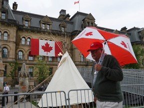 The Office of the Prime Minister and Privy Council is seen behind as a man walks past a large teepee erected by indigenous demonstrators to kick off a four-day Canada Day protest in front of Parliament Hill in Ottawa on Thursday, June 29, 2017. (THE CANADIAN PRESS/Justin Tang)