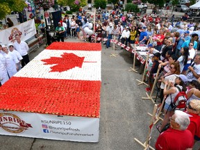 Visitors to the opening day of Sesquifest gather Friday in front of the Canada 150 cake constructed of red-and white-cupcakes at the Covent Garden Market. (MORRIS LAMONT, The London Free Press)