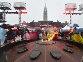 People take shelter from the rain on Parliament Hill as the Centennial Flame burns in Ottawa during Canada 150 celebrations on Saturday, July 1, 2017. THE CANADIAN PRESS/Sean Kilpatrick