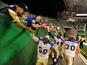 Winnipeg Blue Bombers linebacker Kyle Knox, left, defensive end Tristan Okpalaugo, centre, and offensive lineman Michael Couture, right, celebrate with fans after an overtime win over the Saskatchewan Roughriders at the brand new Mosaic Stadium, in Regina on Saturday, July 1, 2017. THE CANADIAN PRESS/Mark Taylor