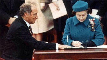 Prime Minister Pierre Elliott Trudeau looks on as Queen Elizabeth II  signs the Proclamation of the Constitution Act in 1982. (File Photo)