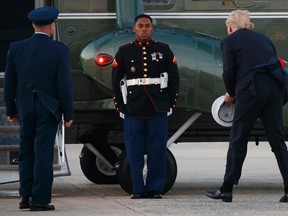 U.S. President Donald Trump retrieves a Marine guards cover after it blew off his head during an arrival at Andrews Air Force Base, Saturday, July 8, 2017, in Andrews Air Force Base, Md. (AP Photo/Evan Vucci)