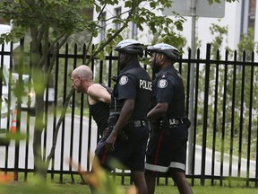 A suspect is escorted in handcuffs by Toronto Police on University Ave. on Monday July 10, 2017. (Veronica Henri/Toronto Sun)