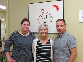 Tamara Cicciarella, left, Kelly Dean and Justin McCourt stand in front of client artwork as they prepare for a Problem Solving and Support group meeting at the AMHS-KFLA main office on Monday. (Ashley Rhamey/For The Whig-Standard)