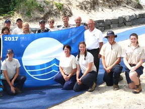 BRUCE BELL/THE INTELLIGENCER
Sandbanks Provincial Park staff surround Environmental Defence Program manager Brett Tryon, Minister of Natural Resources and Forestry Kathryn McGarry, Sandbanks superintendent Robin Reilly and Prince Edward County Mayor Robert Quaiff with the Out Beach Blue Flag at outlet Beach on Wednesday morning. Sandbanks became just the second provincial park in Ontario with a beach to receive the international Blue Flag designation.