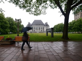 A pedestrian walks in the rain past the Supreme Court of Canada in Ottawa on Friday, June 23, 2017. THE CANADIAN PRESS/Sean Kilpatrick