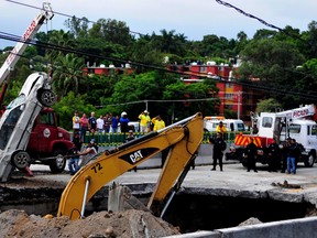 Rescue workers use a crane to lift a vehicle that drove into a sinkhole on a highway in Cuernavaca, Mexico, Wednesday, July 12, 2017. A father and son were killed when the deep sinkhole swallowed their car on Wednesday morning. Civil protection rescuers reached the rubble-covered Volkswagen Jetta lying on its roof at the bottom of the hole in the afternoon, after working for more than eight hours on the closed section of road. (AP Photo/Tony Rivera)