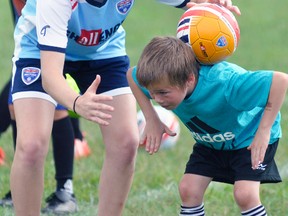 Instructor Caitlin Walker (left) assists Tyler Otten-Murray with a trick of flipping the soccer ball up over his head and keeping it behind his neck during the Challenger Sports British Soccer camp last Wednesday, July 12. ANDY BADER/MITCHELL ADVOCATE