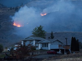 THE CANADIAN PRESS/Darryl Dyck 
A wildfire burns on a mountain in the distance behind a house that remains standing on the Ashcroft First Nation, near Ashcroft, B.C., late Sunday July 9, 2017.