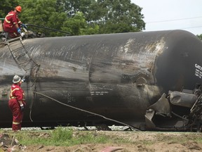 Workers attach a hose to a derailed tank car as cleanup efforts continued Thursday, a day after 13 cars of a 120-unit CN freight derailed near downtown Strathroy. (Mike Hensen/The London Free Press)