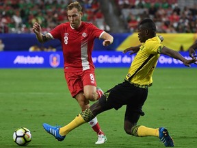 Canada's Scott Arfield (L) is tackled by Jamaica's Cory Burke (C) during their quarterfinal match of the 2017 CONCACAF Gold Cup at the University of Phoenix Stadium on July 20, 2017 in Glendale, Arizona. Jamaica won 2-1.