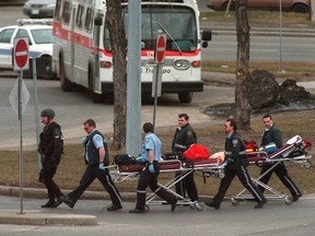 A tactical police officer escorts emergency workers rushing to bring stretchers to the shooting victims at OC Transpo’s headquarters on St. Laurent Boulevard in 1999.