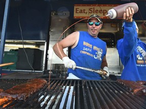 Jame Stoddart watches Jamie Breault squirt sauce onto his ribs barbecuing over a wood fire at Boss Hogs, one of the rib venders during Ribfest at K-Days in Edmonton, July 23, 2017. Ed Kaiser/Postmedia