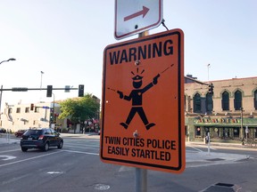 A fake street sign is mounted on the same pole as legitimate ones at the intersection of Cedar and Riverside Aves. Sunday, July 23, 2017, in Minneapolis. The fatal shooting of an Australian woman by a Minneapolis police officer has sparked the posting of at least two fake street signs warning people of "easily startled" officers. The Star Tribune reports the signs were spotted this weekend, one in Minneapolis and one in St. Paul. The official-looking orange metal sign reads: "WARNING: TWIN CITIES POLICE EASILY STARTLED." (Erin Adler/Star Tribune via AP)
