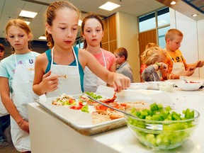 Luke Hendry/The Intelligencer
Gabrielle Taylor prepares her mini pizza while Ella Harrow, left, and Jessica Shea wait their turns during the Food for Thought cooking course Monday.