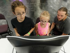 Marc Leveille and his two daughters Mhalia (centre), 6, and Khym (left), 9, play game developer Mike Mattai's game Voxeltron: 1982 at the GDX Game Discovery Exhibition inside the TechLife hall at K-Days at Northlands in Edmonton on Tuesday, July 25, 2017. Ian Kucerak / Postmedia