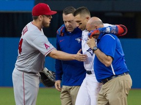 Toronto Blue Jays' Troy Tulowitzki gets a consoling pat from L.A. Angels first baseman C.J. Cron, left, as he is helped off the field by trainers during an MLB game in Toronto on July 28, 2017. (THE CANADIAN PRESS/Fred Thornhill)