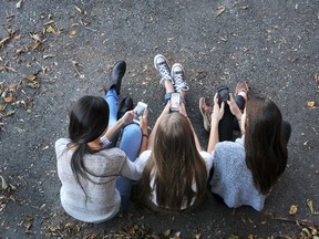 In this stock photo, teenage girls look at their cellphones while sitting outside. (Getty Images)