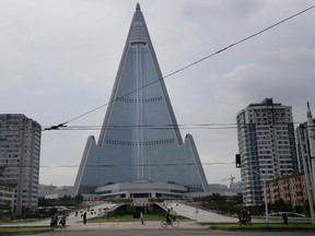 In this Friday, July 28, 2017, photo, people walk past the 105-story pyramid shaped Ryugyong Hotel in Pyongyang, North Korea. Walls set up to keep people out of a construction area around the gargantuan Ryugyong Hotel were pulled down as the North marked the anniversary of the Korean War armistice to reveal two broad new walkways leading to the building and the big red propaganda sign declaring that North Korea is a leading rocket power. (AP Photo/Wong Maye-E)