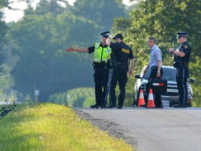 OPP investigators and the coroner survey the scene on Sinclair Drive west of Bear Creek Road where a cyclist died after being hit by a car Tuesday. The bike can be seen in the grass at left. (MORRIS LAMONT, The London Free Press)