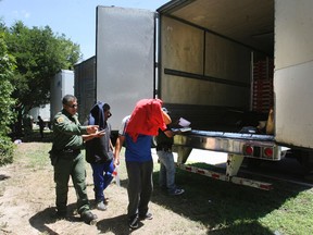 In this Sunday Aug. 13, 2017, photo, Border Patrol officers escort a group of immigrants to a van after a group was found in the tractor-trailer in Edinburg, Texas. Police in Texas acting on a tip found the immigrants locked inside the tractor-trailer parked at a gas station about 20 miles (30 kilometers) from the border with Mexico, less than a month after 10 people died in the back of a hot truck with little ventilation in San Antonio. (Delcia Lopez/The Monitor via AP)