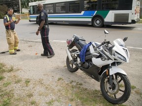 A firefighter explains the position of the motorcycle to a police officer after a crash at Huron Street and Oakville Avenue Wednesday. Witnesses say the motorcyclist lost control after a black car turned left in front of him, and sped away. (MIKE HENSEN, The London Free Press)
