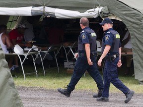 Members of the CBSA walk by a tent housing asylum seekers at the Canada-United States border in Lacolle, Que. Thursday, August 10, 2017. THE CANADIAN PRESS/Graham Hughes