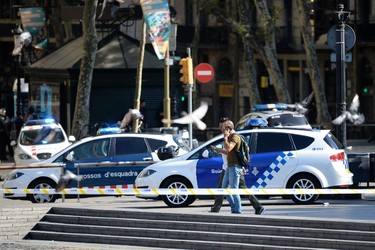 Plain-clothes policemen phone as they walk past police cars in a cordoned off area after a van ploughed into the crowd, injuring several persons on the Rambla in Barcelona on August 17, 2017. / AFP PHOTO / Josep LAGOJOSEP LAGO/AFP/Getty Images