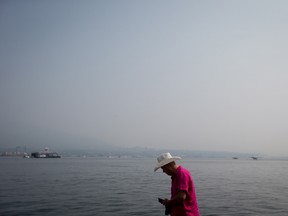 Smoke from wildfires burning in central British Columbia hangs in the air as a man walks on a dock in Vancouver, B.C., on Thursday August 10, 2017.