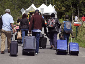 A family from Haiti approach a tent in Saint-Bernard-de-Lacolle, Quebec, stationed by Royal Canadian Mounted Police, as they haul their luggage down Roxham Road in Champlain, N.Y., Monday, Aug. 7, 2017. CHARLES KRUPA / ASSOCIATED PRESS