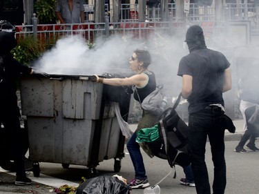 Counter-protesters wearing masks push a smoking trash bin as another counter-protester tries to stop them in a demonstration against far-right group La Meute on Sunday, Aug. 20 in Quebec City. (Dave Sidaway/Postmedia)