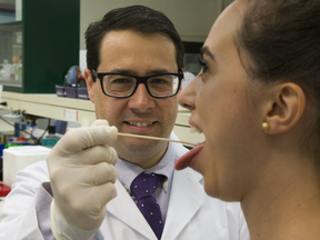 Dr. Walter Siqueira swabs a sample of saliva from graduate student Camilla Esteves in his laboratory at Western University in London on Tuesday. Siqueira is developing a saliva test for Zika virus. (Derek Ruttan/The London Free Press/Postmedia Network)