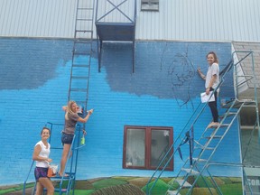 Carly Neilson (left) and St. Patrick's Catholic High School teacher Kelly Gordon encourage artist Jorrie Kirby in the middle of her mural on the wall of St. Vincent De Paul Food Bank. (Photo courtesy of Sarnia Police)