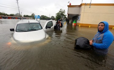 Conception Casa, center, and his friend Jose Martinez, right, check on Rhonda Worthington after her car became stuck in rising floodwaters from Tropical Storm Harvey in Houston, Texas, Monday, Aug. 28, 2017. The two men were evacuating their home that had become flooded when they encountered Worthington's car floating off the road. (AP Photo/LM Otero) ORG XMIT: TXMO107