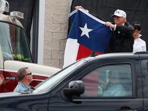 President Donald Trump, accompanied by first lady Melania Trump, holds up a Texas flag after speaking with supporters outside Firehouse 5 Corpus Christi, Texas, Tuesday, Aug. 29, 2017, following a briefing on Harvey relief efforts. (AP Photo/Evan Vucci)