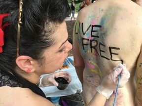 In this Sept. 10, 2016, file photo, artist Nicole Tossas paints a slogan on the back of a bicyclist before the annual Philly Naked Bike Ride in Philadelphia. Organizers of the Philly Naked Bike Ride said Tuesday the ninth annual event will take place throughout the city's streets Sept. 9, 2017. (AP Photo/Dino Hazell, File)