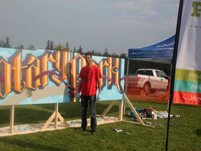 AJA Louden, an Edmonton-based visual artist, stands before his spray paint exhibit during Arts in the Park at Rotary Park on Aug. 23 (Jeremy Appel | Whitecourt Star).