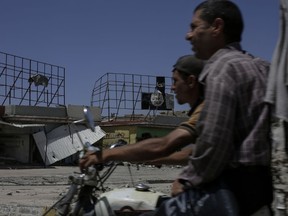 In this Saturday, May 13, 2017 file photo, two men carrying a white flag on their motorbike pass an Islamic State militant banner in western Mosul. (AP Photo/Bram Janssen, File)