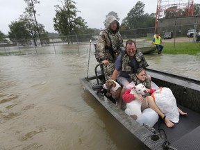 In this Monday, Aug. 28, 2017, file photo, John and Kathy Cservek hold their dogs Lacy and Iggy while being rescued from their home as floodwaters from Tropical Storm Harvey rise in Spring, Texas. The couple saw their dream house in suburban Spring devastated only a little over a year after they bought it. (AP Photo/David J. Phillip, File)