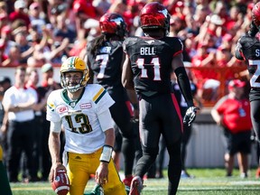 Edmonton Eskimos' quarterback Mike Reilly, left, picks himself up after being sacked by Calgary Stampeders' Junior Turner, centre, and teammate Josh Bell during second half CFL football action in Calgary, Monday, Sept. 4, 2017.