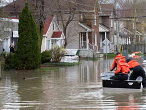 A woman surveys the flooding in front of her home as fire fighters use a boat to access residents in the area of Rue St-Louis and Rue Rene in the old section of Gatineau on May 12, 2017.