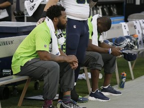 This Thursday, Aug. 31, 2017 file photo Seattle Seahawks defensive end Michael Bennett, left, sits during the playing of the national anthem next to Justin Britt, centre, and another teammate before a preseason game in Oakland, Calif. (AP Photo/Eric Risberg,File)