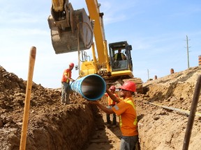 Mike Needham lowers a 6.1-metre length of 400mm plastic water pipe into  its trench with the guidance of Trent Heuvel, left, Chuck Zettler, front and Joe Amaral, right at rear. CH Excavating has a $6-million contract to grade land and install sewer and water services for the new, 120-lot Silverleaf subdivision. (MIKE HENSEN, The London Free Press)