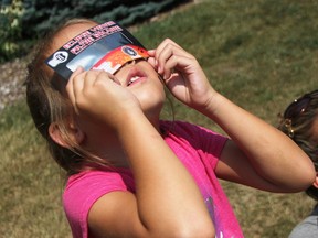 Aly Lee, 5, checks out a partial eclipse of the sun from outside the Bright's Grove Library Aug. 21. Steeves and Rozema is collecting gently used pairs of eclipse glasses until Sept. 17 to donate to Astronomers Without Borders. Tyler Kula/Sarnia Observer/Postmedia Network