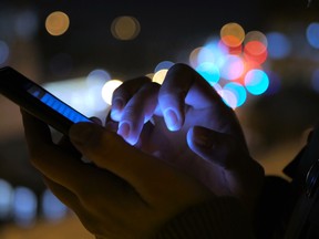 In this stock photo, a woman uses a smartphone at night on a street. (Getty Images)