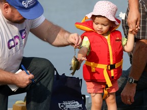 Tim Miller/The Intelligencer
Two-year-old Kensley Newlands of Stirling reaches out for her freshly-caught fish as Belleville Police Service Auxiliary member, Leigh McCormick, gets ready to measure it during the annual Cops and Kids Fishing Derby at Victoria Park on Saturday in Belleville. The derby, which is normally held in June, had to be rescheduled to September due to heavy flooding which closed down Victoria Park at the start of the season.