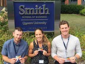 Former Olympians, from left, rower Mike Braithwaite, heptathlete Jessica Zelinka and rower Will Dean display their Queen’s University student cards outside the Smith School of Business, where the three are students in the Master of Entrepreneurship and Innovation program. They are attending school on scholarships provided by the Canadian Olympic Committee. (Submitted photo)