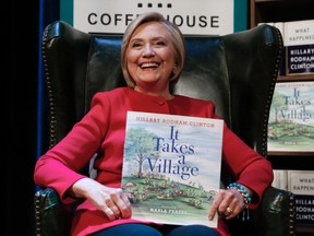 Hillary Clinton holds her book "It Takes A Village" as she sits on stage at the Warner Theatre in Washington during a book tour event for her new book "What Happened" hosted by the Politics and Prose Bookstore on Monday, Sept. 18, 2017. (Carolyn Kaster/AP Photo)