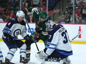 Wild forward Marcus Foligno tries to shove the puck between the pads of Jets goalie Connor Hellebuyck while being defended by the Jets’ Ben Chiarot in Minneapolis last night.The Wild won 1-0. (AP)