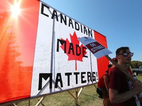 Unifor workers picket in the shade of a huge Canadian flag erected at the entrance at Cami in Ingersoll on a warm Friday afternoon on Friday September 22, 2017. (MIKE HENSEN, The London Free Press)